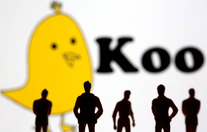 Silhouetted toy figures of people stand in front of the Koo app&#x27;s logo