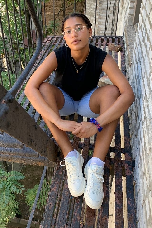 model wears white Reebok vintage-style sneakers with purple bike shorts and a black tee