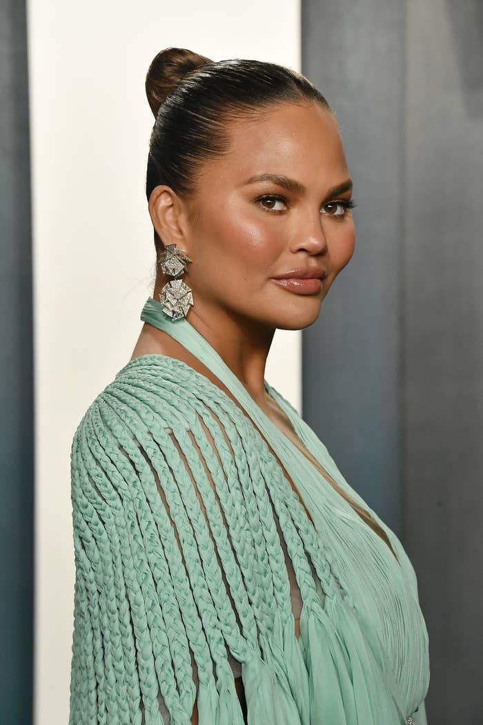 Chrissy Teigen at the 2020 Vanity Fair Oscar Party wearing a braided dress, long earrings, and her hair up in a bun