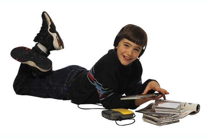 A kid laying on the floor looking at CDs while listening to his CD walkman 