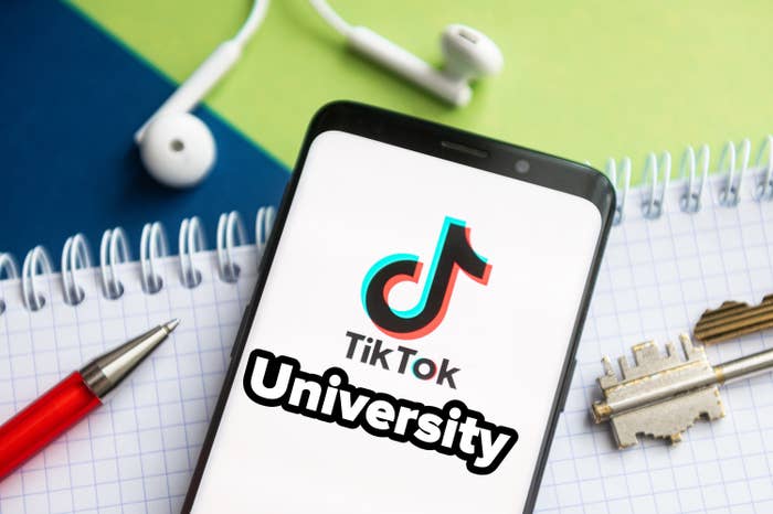 TikTok University on a smartphone which is on top of a notepad next to a pen, key, and earphones
