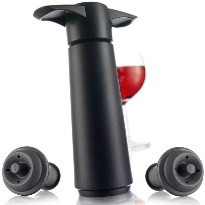 The wine save pump sitting in front of a glass of red wine next to two wine stoppers 