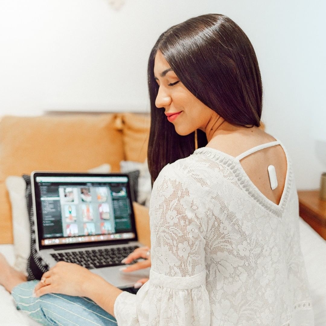 A person wearing the posture trainer while sitting on a bed in front of a laptop 