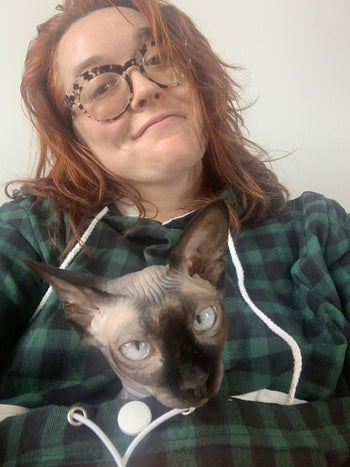 BuzzFeed writer wearing the sweatshirt with hairless cat sitting inside pouch 