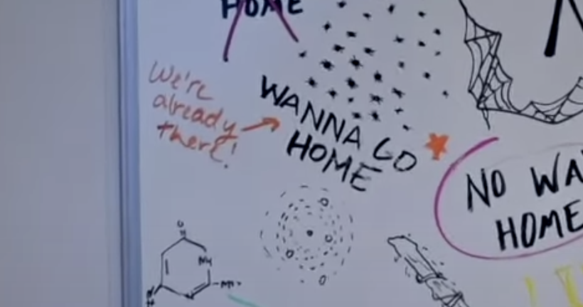 A close-up of the whiteboard reading &quot;Wanna Go Home&quot; and someone drawing an arrow and writing, &quot;We&#x27;re already there&quot;