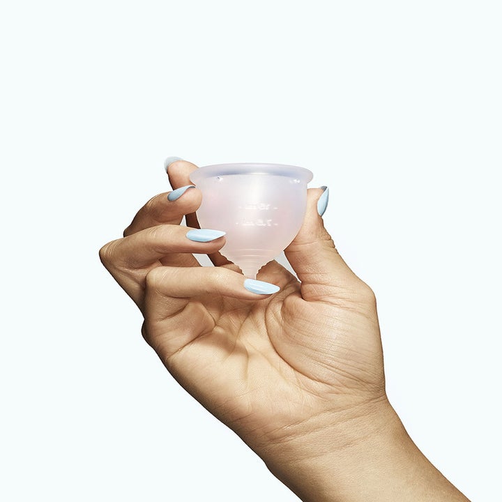 A hand holding a clear menstrual cup 