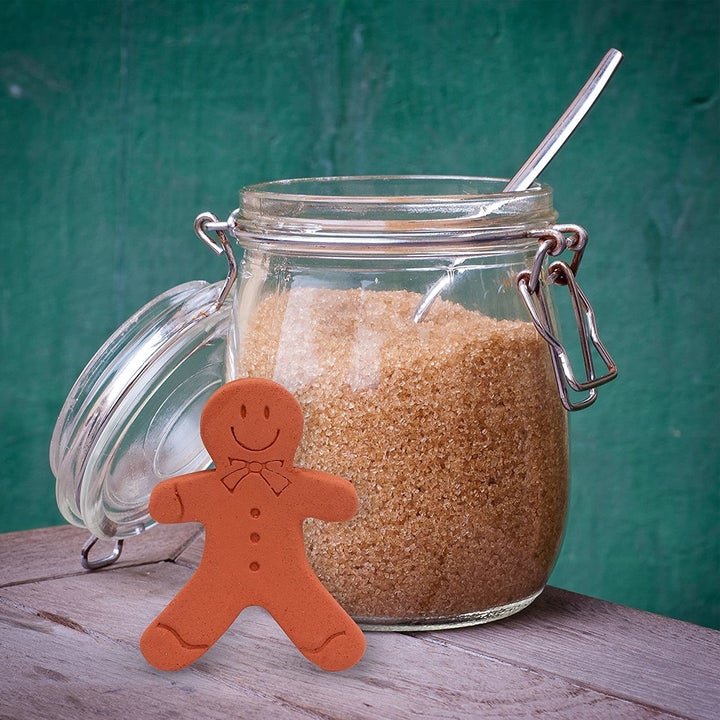 A brown clay gingerbread man figure sitting next to an open glass container of brown sugar 