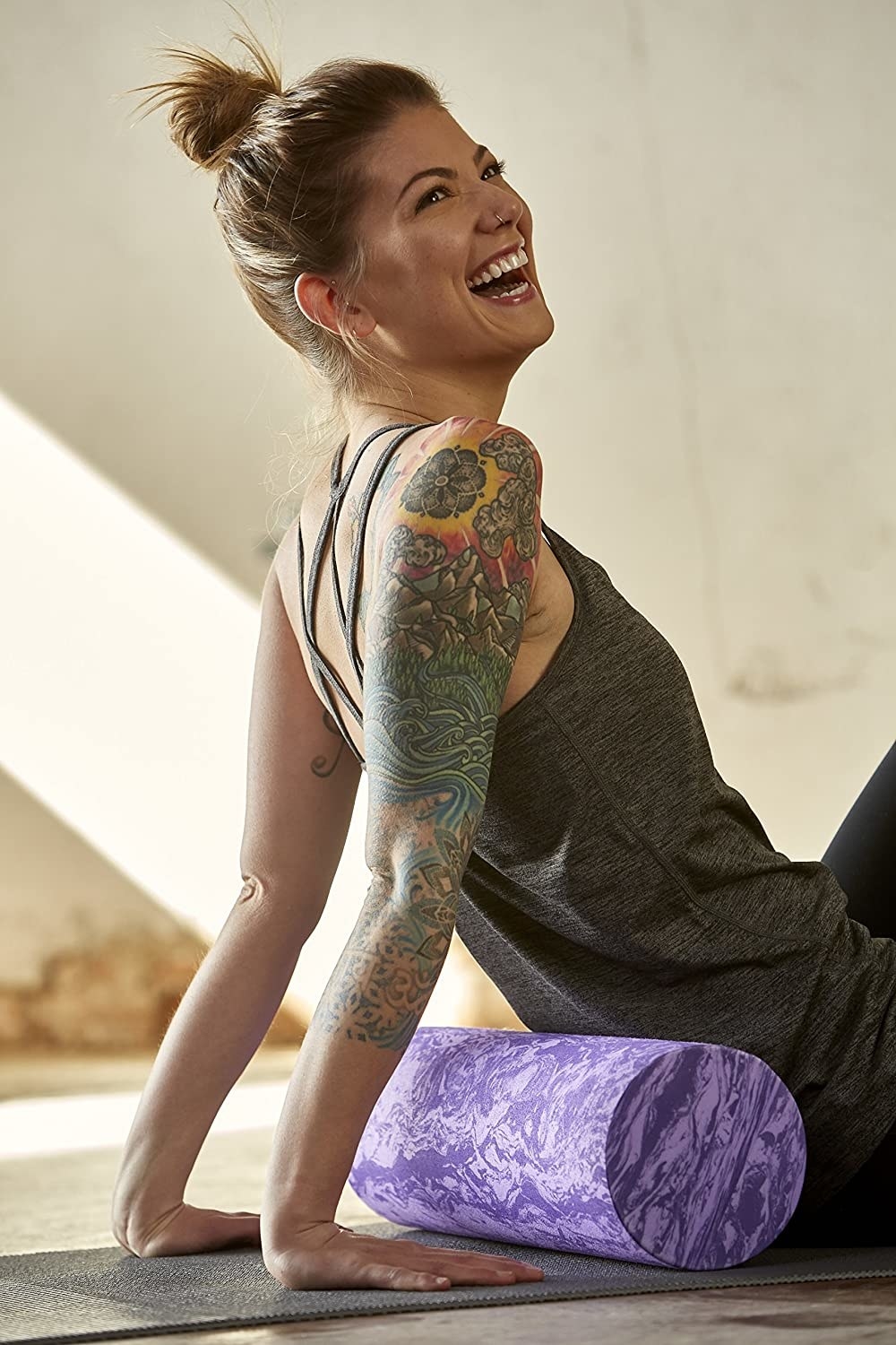 A smiling person using the foam roller while sitting on a yoga mat