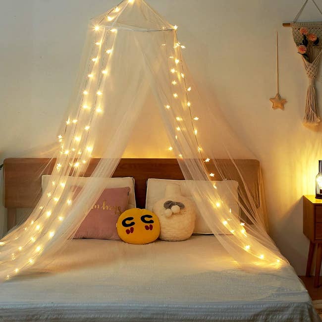 Sheer white canopy over bed with glowing star lights draped on either side 