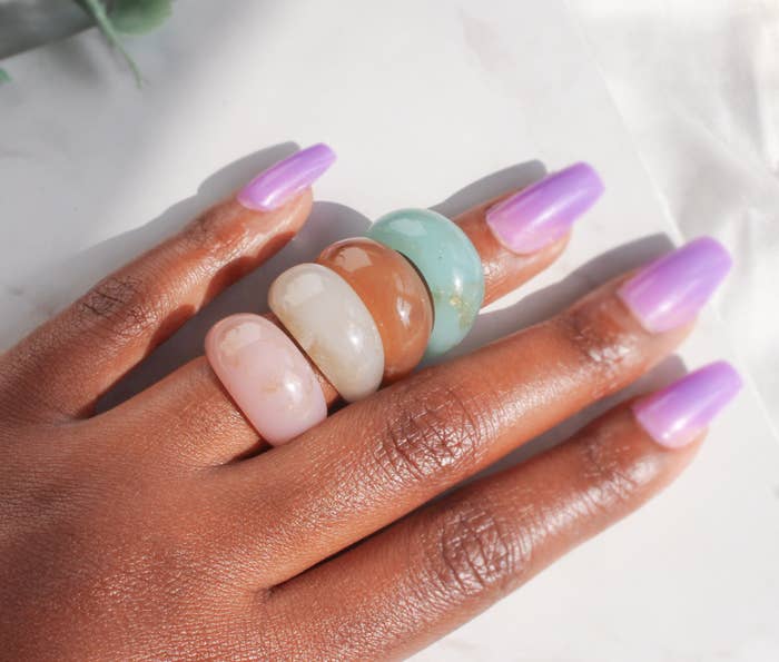 model&#x27;s hand with pink, white, brown, and turquoise stone-like rings