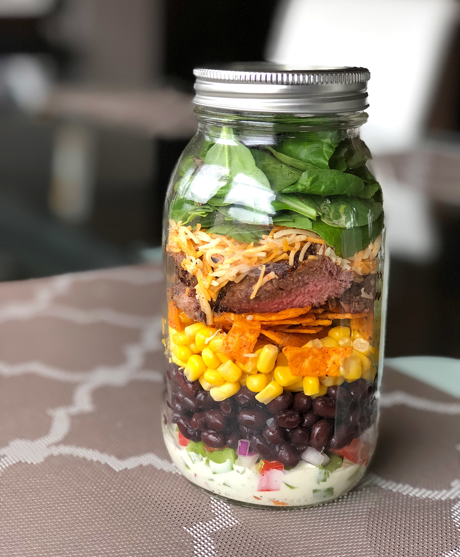 A close up of a neatly layered Tex Mex style salad in a mason jar