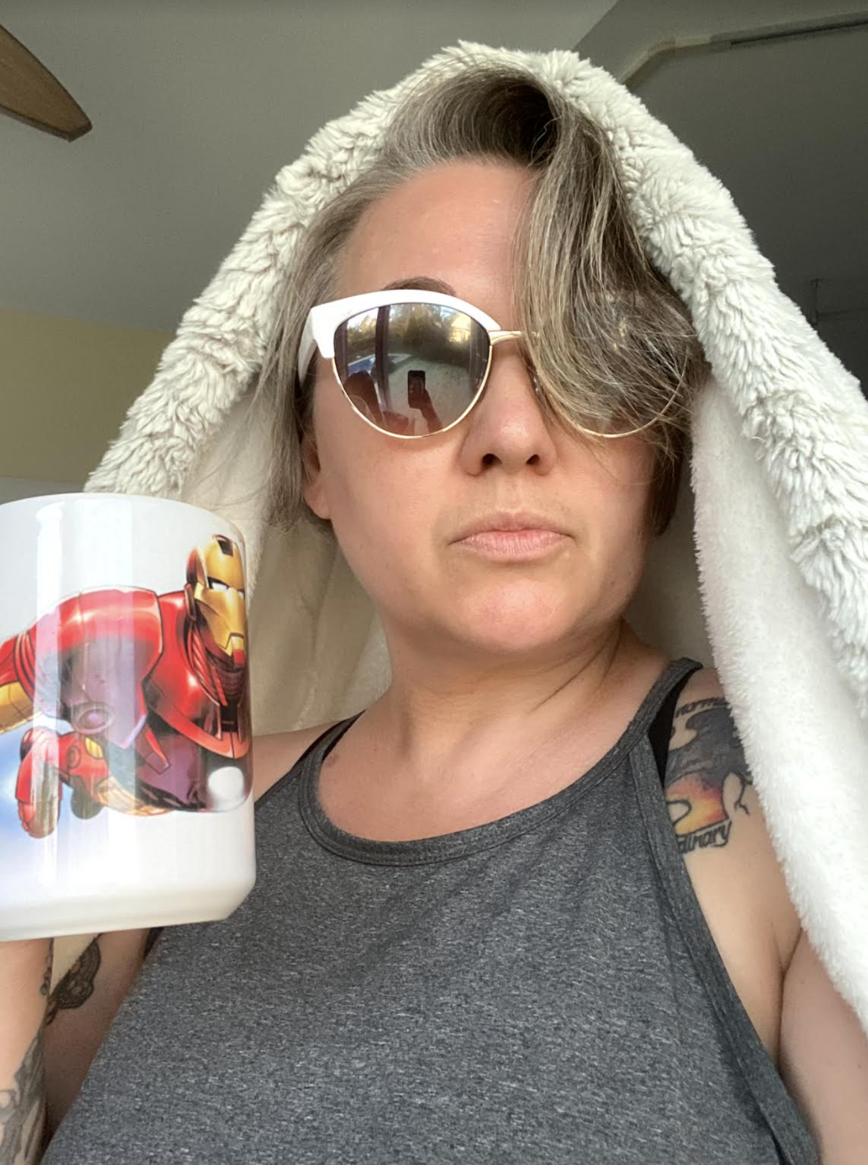 Cayce wearing sunglasses and a blanket over her head while holding a coffee mug with Iron Man on it