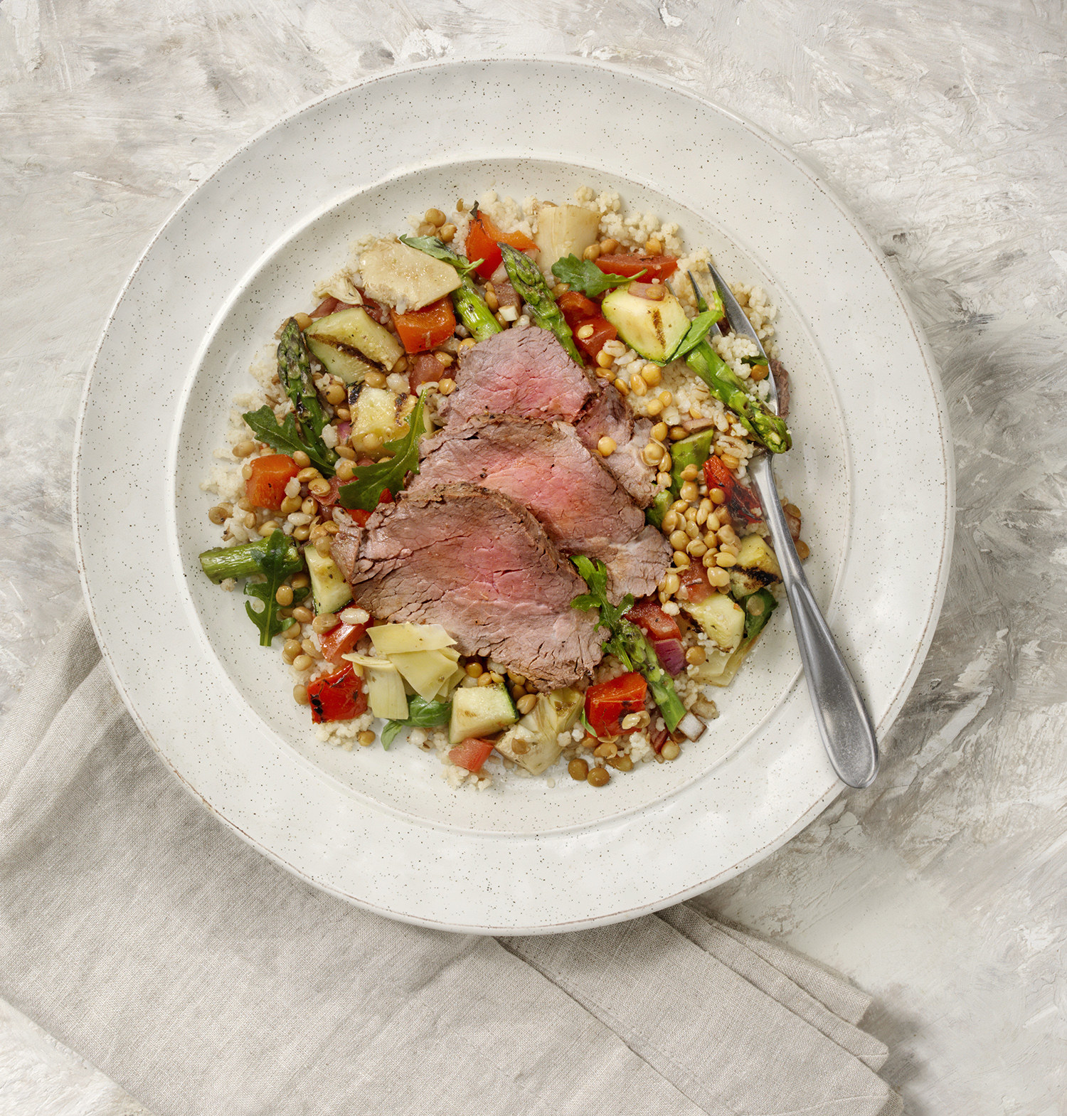 A top down view of a fresh lentil salad with thinly sliced rare roast beef