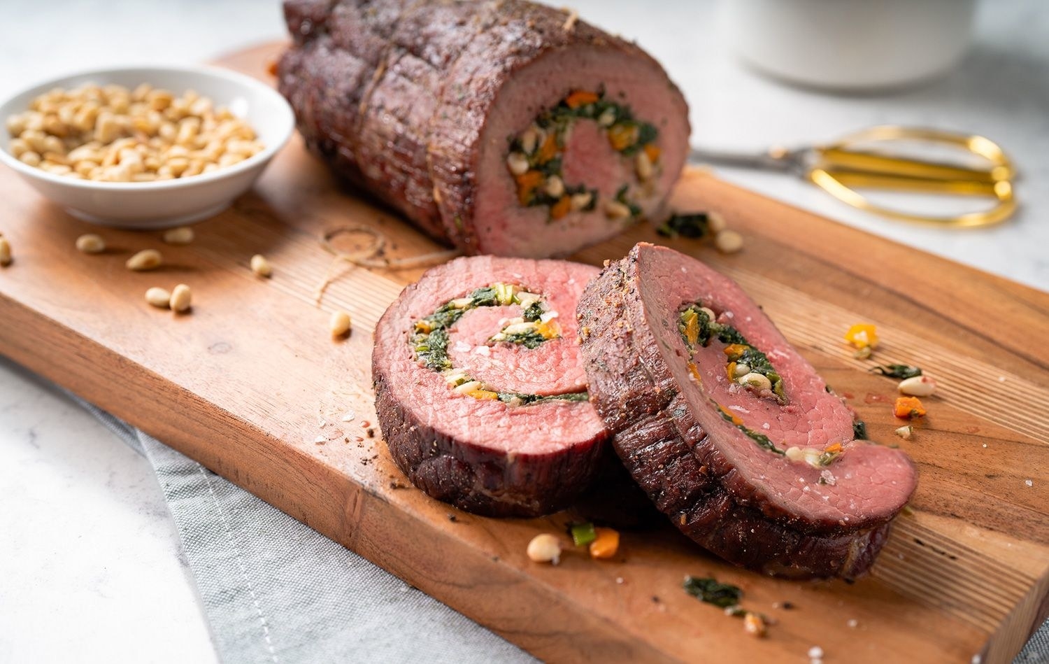 A large stuffed and rolled roast beef sliced and arranged on a wooden serving platter