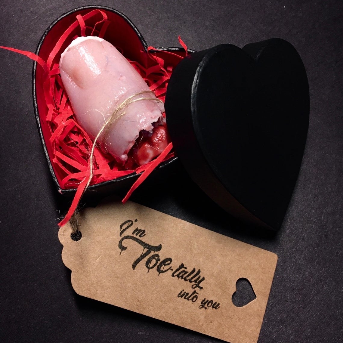 Black heart-shaped box with a realistic looking severed toe inside and a card that says &quot;I&#x27;m toe-tally into you&quot; 