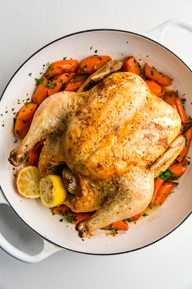 A whole roast chicken over carrots.