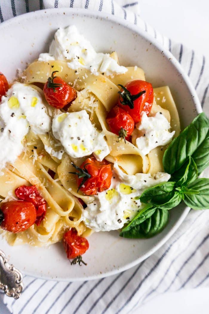 A plate of pasta with cherry tomatoes, burrata, and basil.