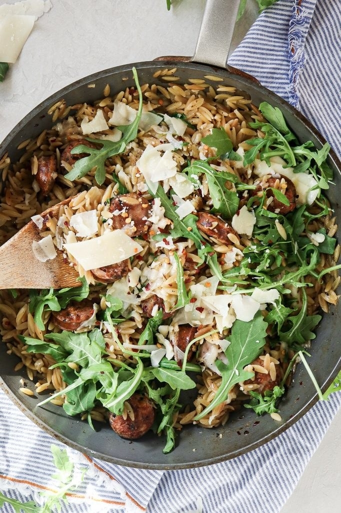 A skillet with orzo, arugula, and chicken sausage.