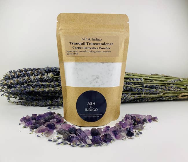 a bag of carpet refresher powder next to purple stones and sprigs of lavender