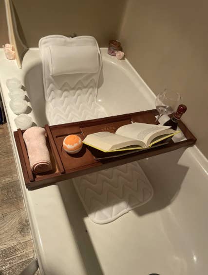 a reviewer photo of the cushion in the tub with a bath tray and bath bomb