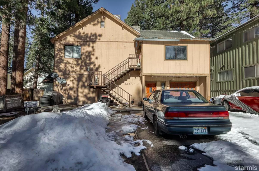 A car sits in the large driveway and the home has few trees off to the side