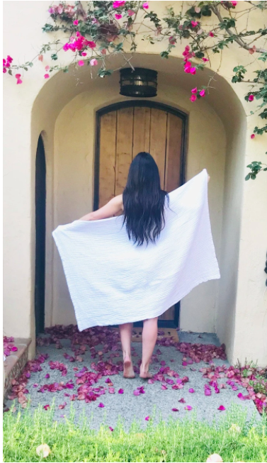 a model walking outside wearing the white bath sheet with flower petals on the ground