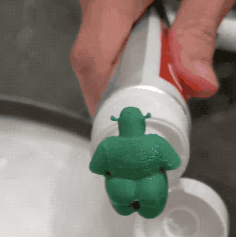 gif of a plastic limbless shrek on a tube of toothpaste with the toothpaste coming out of its butt onto the toothbrush 