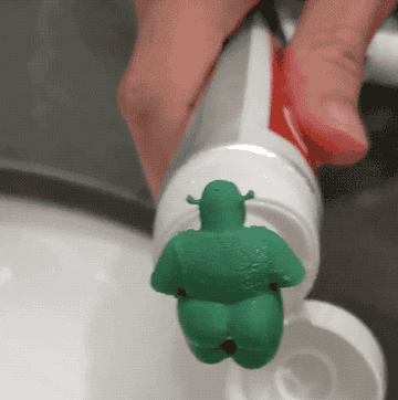 gif of a plastic limbless shrek on a tube of toothpaste with the toothpaste coming out of its butt onto the toothbrush 