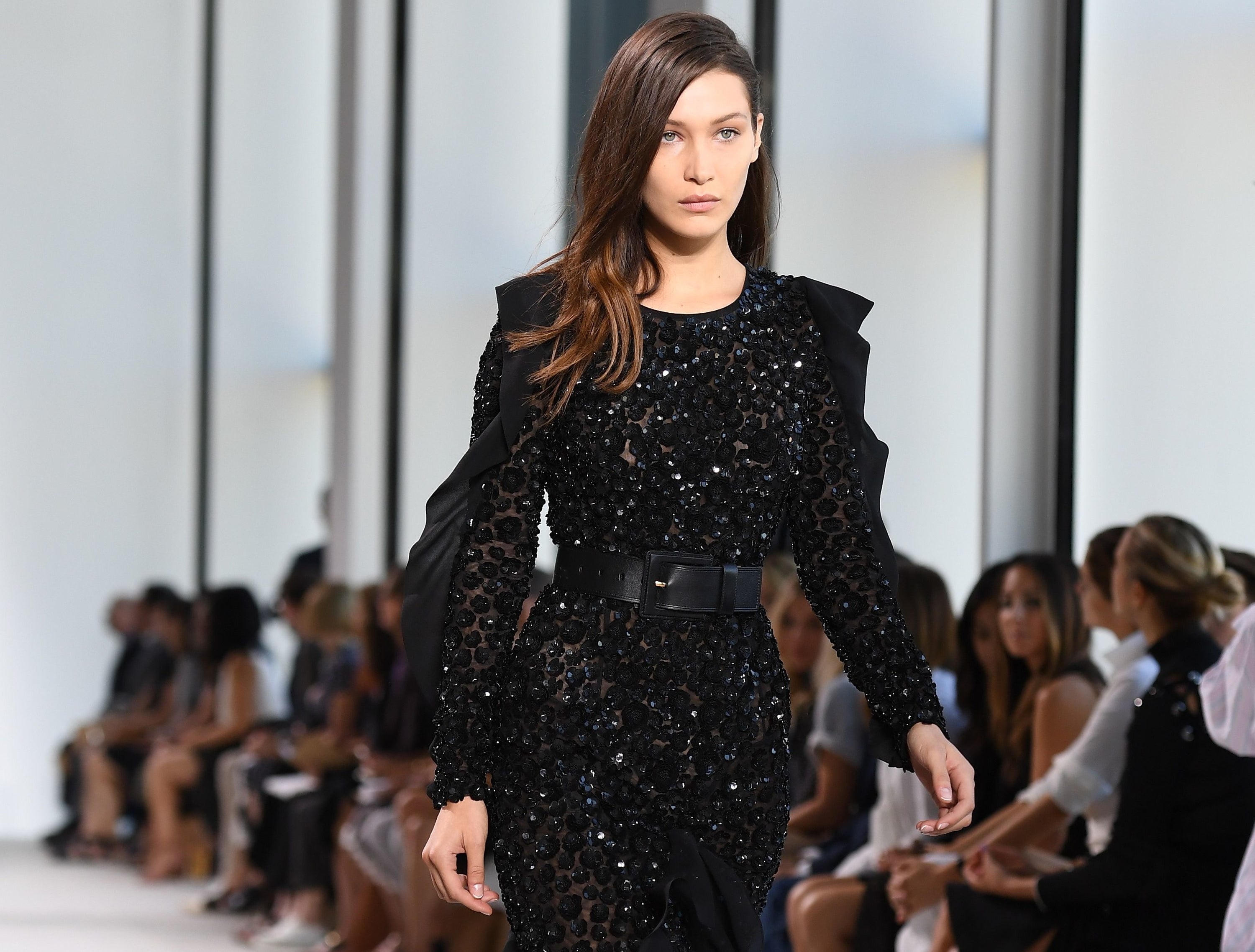 Bella walks in the Kors show in a black sequined long sleeve dress cinched with a black belt 