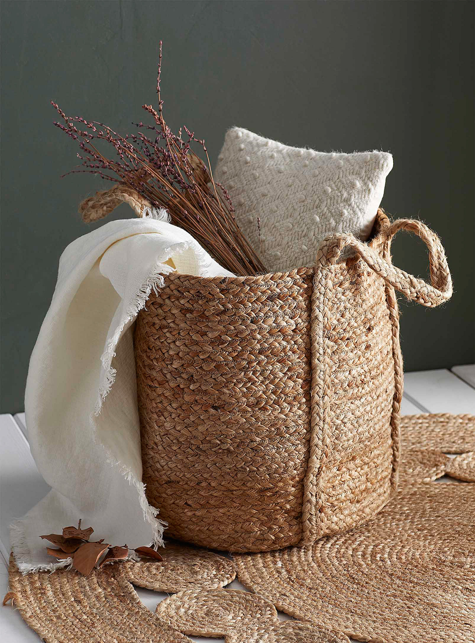 A woven basket filled with pillows, blankets, and dried flowers