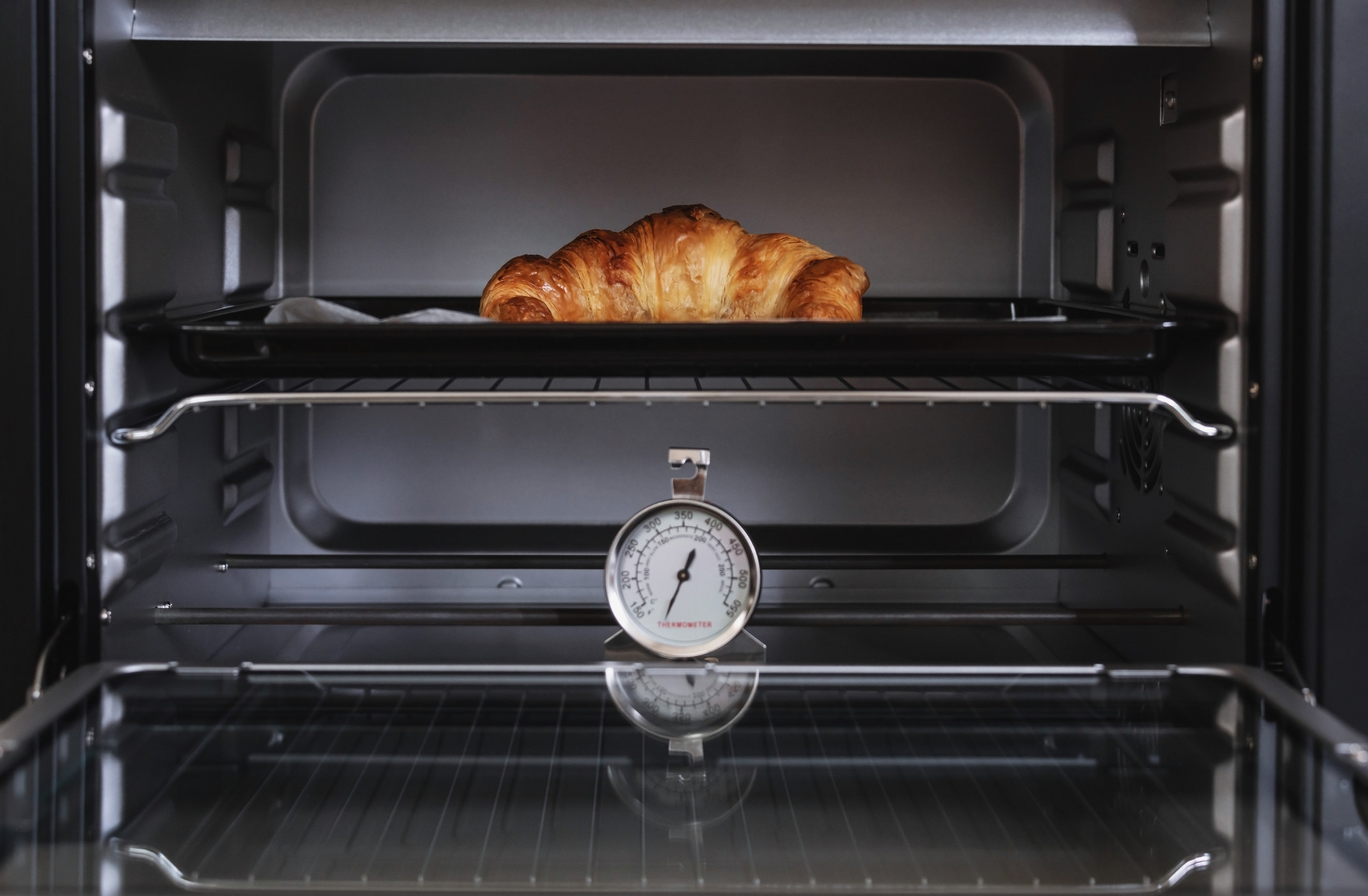 An oven thermometer in the oven as a croissant bakes