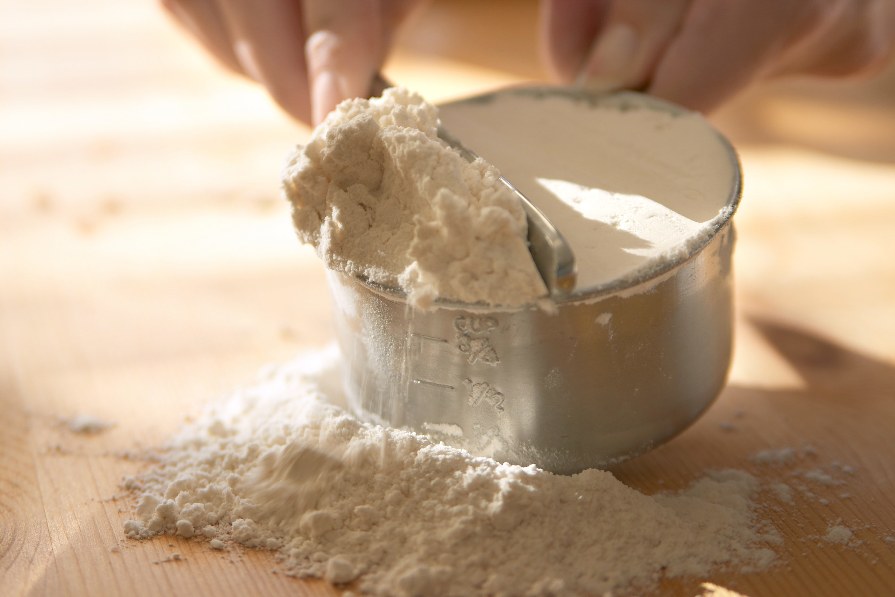A person leveling off flour into a measuring cup