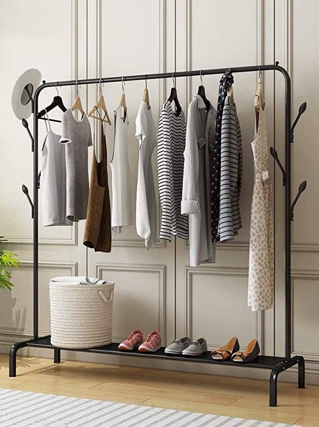 Black metallic hanging rack with clothes and shoes on it.