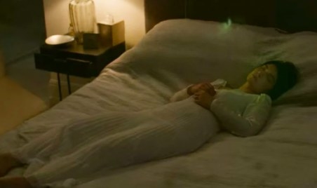 Adele lies with her eyes closed on a bed, a green light floats above her