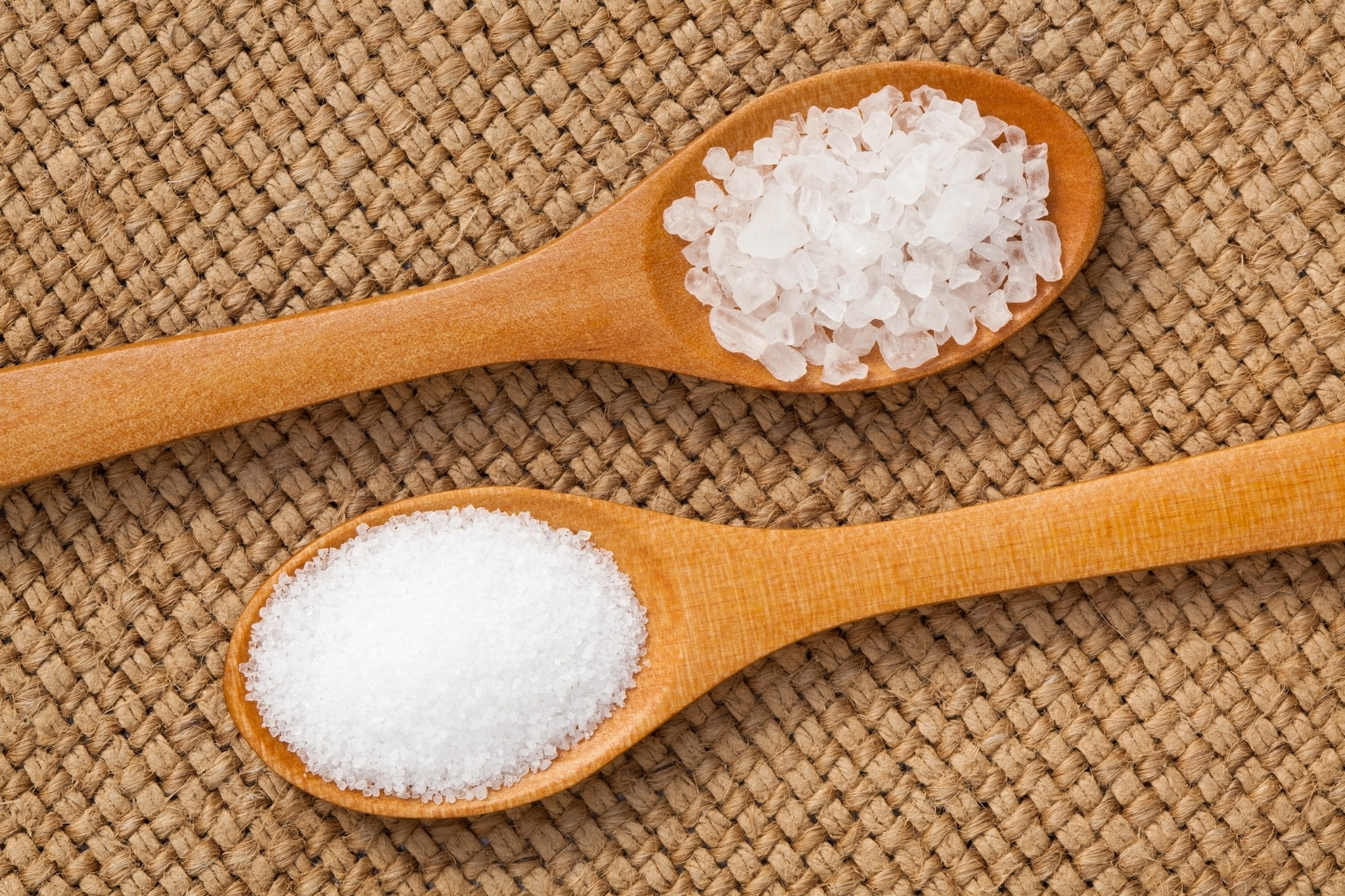 Coarse salt on a wooden spoon and finer salt on a wooden spoon