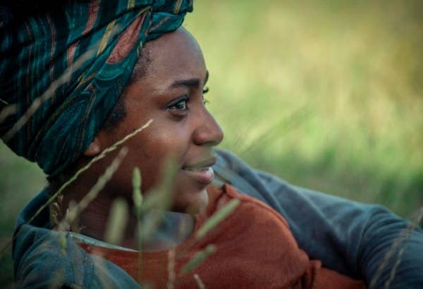 Louise lies back in grass; she is smiling and has her hair tied back in a headscarf