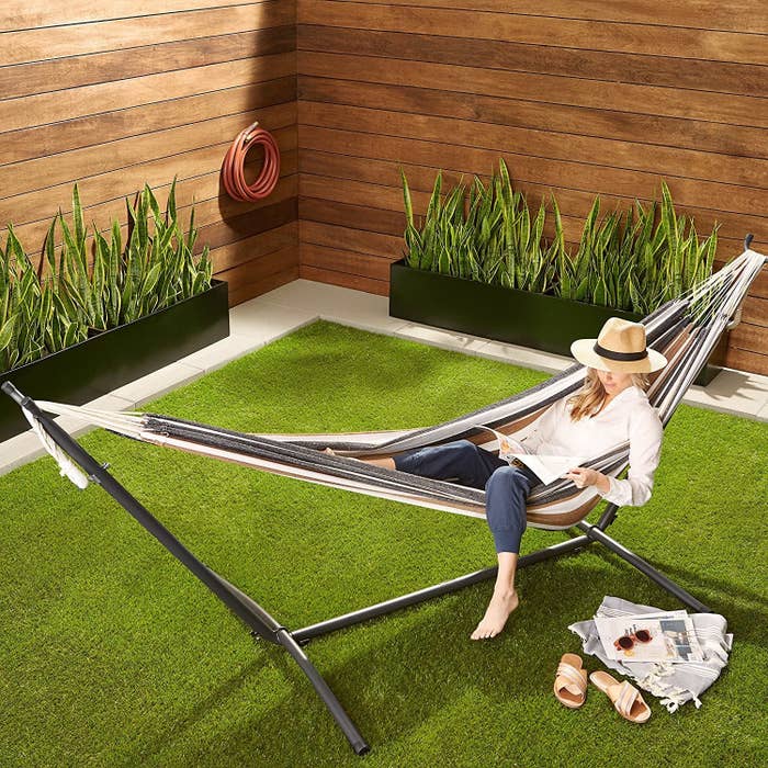 A person lying in the hammock in an enclosed garden and reading.