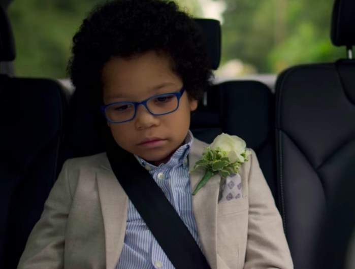 Adam sits in the backseat of a car wearing wedding atire and looking sad