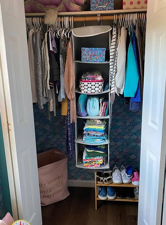 reviewer pic of the five-tier hanging shelf with three mesh pockets on the side hanging in a closet in a bedroom