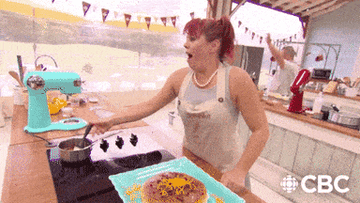 An animated image of a woman throwing her hands up into the air after finishing baking.