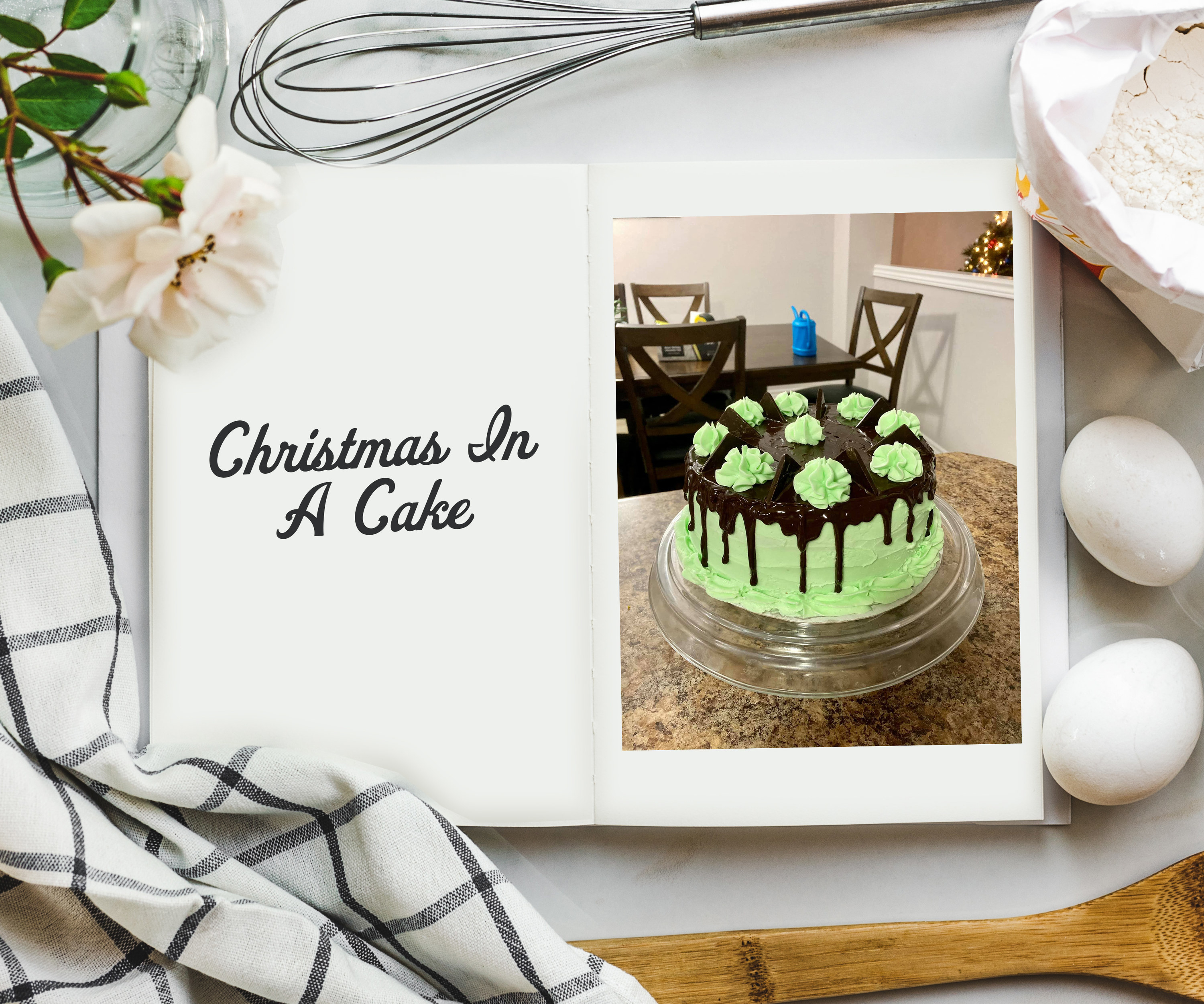 An overhead shot of cookbook on a table surrounded by ingredients and a photo on the inside of a lime green cake on a cake-stand covered with chocolate ganache on top and piped green florets. 