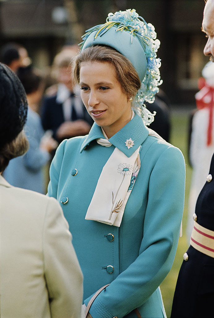 A young Princess Anne wearing a decorated pill box hat as she listens to someone speak