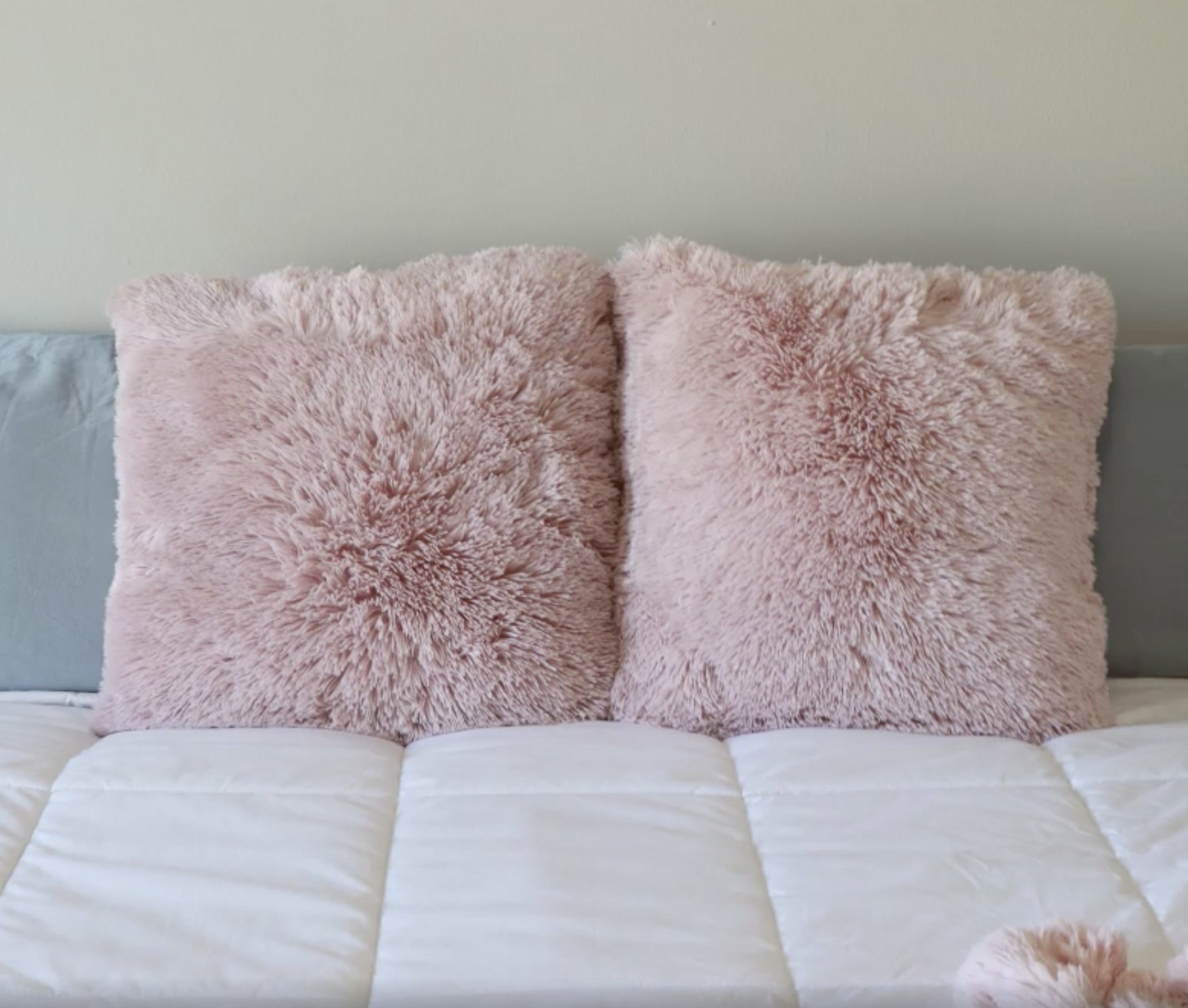 Two pink faux fur throw pillows on a bed