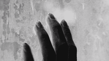 A close-up of a hand touching a frosted window
