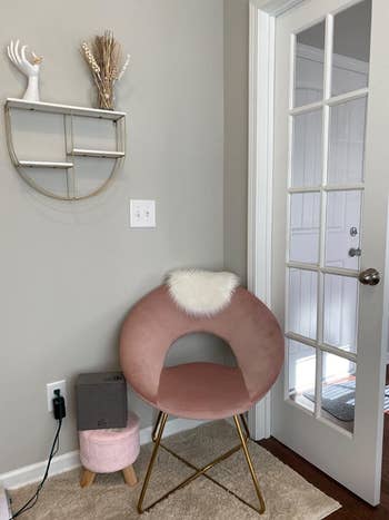 A reviewer showing their pink chair in the corner of a room