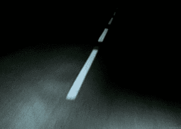 A dark road at night, lit only a few feet by a car&#x27;s headlights