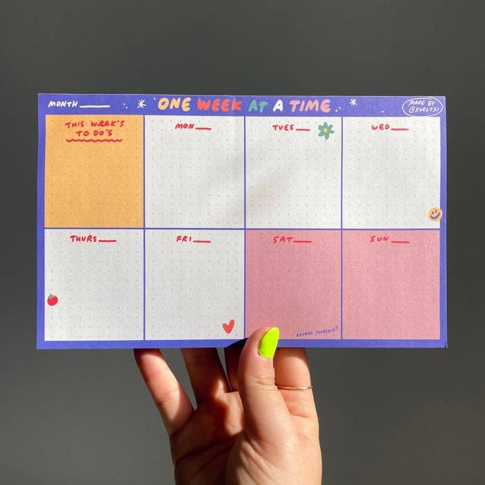 hand holds up a small planner that says one week at a time with room for each day of the week plus an area for this week&#x27;s to-dos