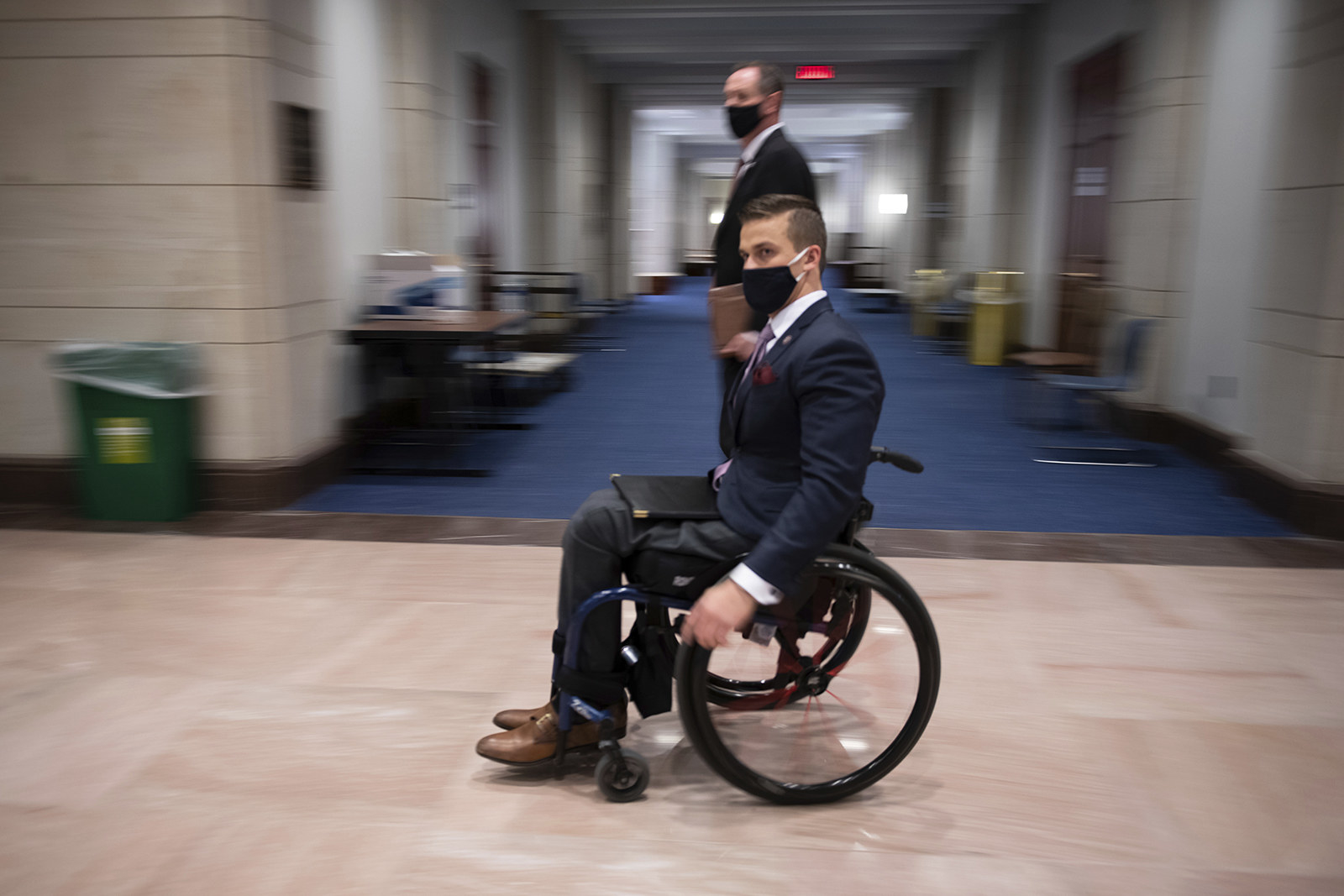 Cawthorn wears a suit and sits in a wheelchair against a blurred background in a Capitol corridor