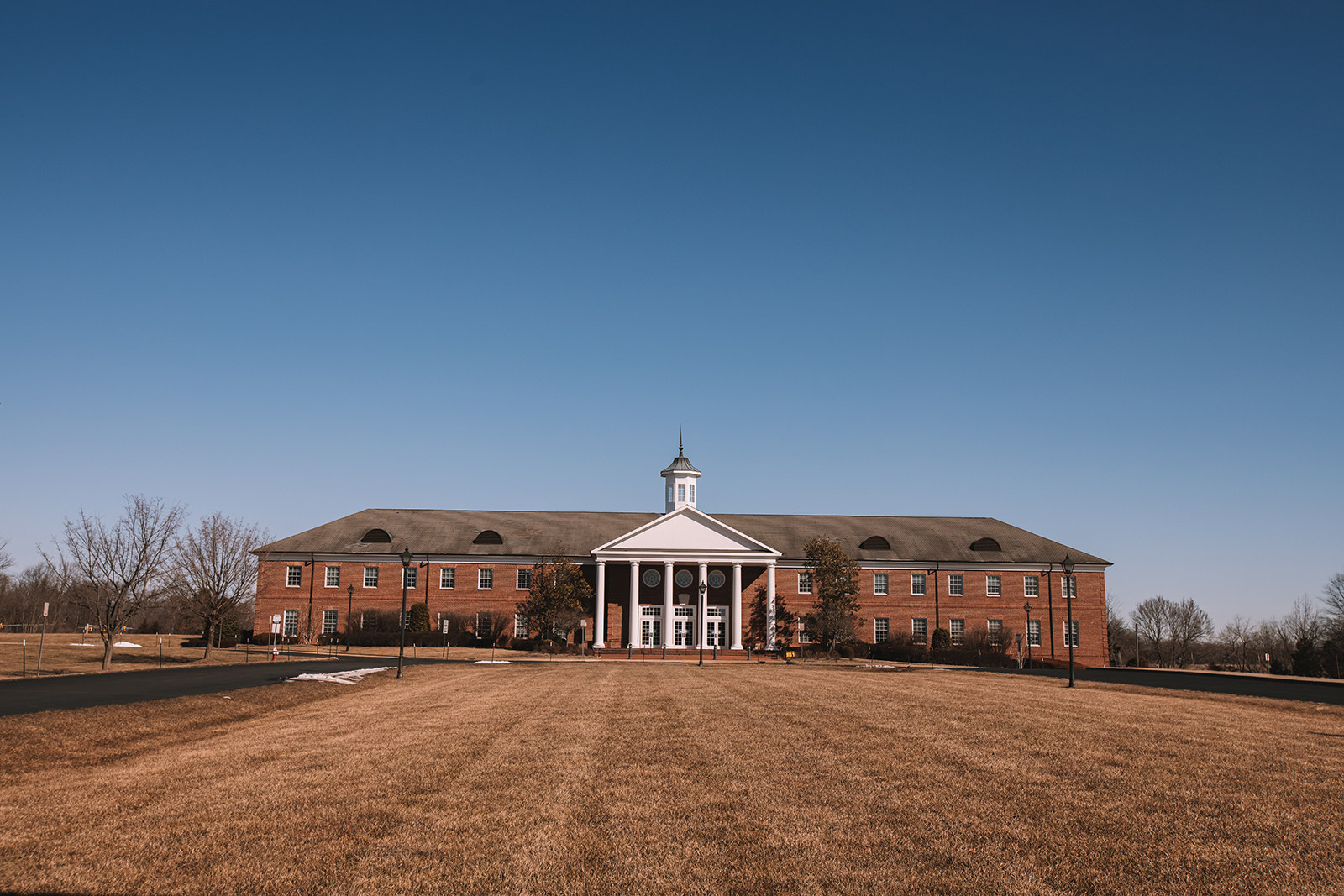 A large brick building with columns stands in the distance at the end of a grassy field