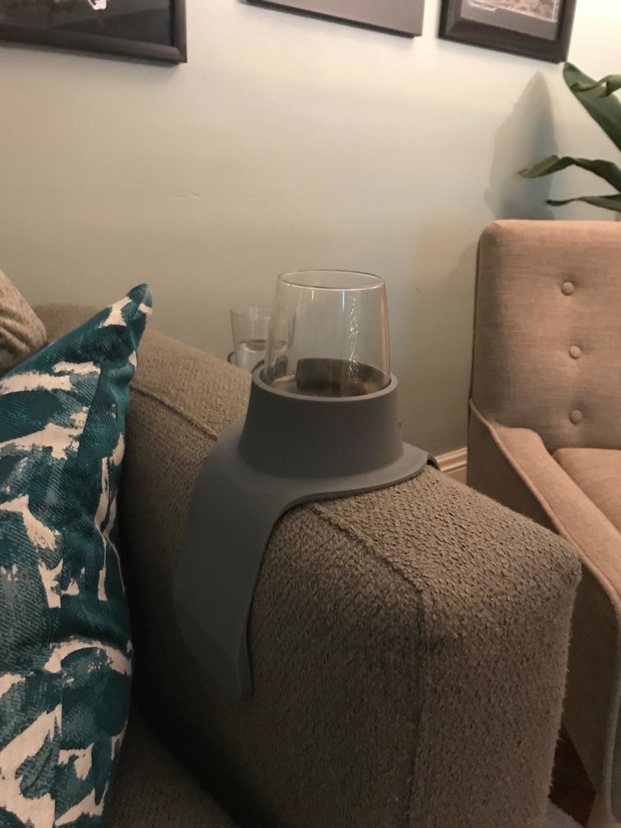 reviewer image of the grey couch coaster on a couch arm with a glass resting inside of it